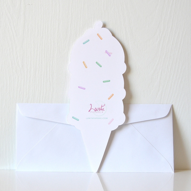 Puede incluir: Un sobre blanco con una tarjeta de cono de helado rosa, blanco y azul con chispas en la parte superior. La tarjeta dice "Lunita Papeleria" y "lunitapapeleria.com".