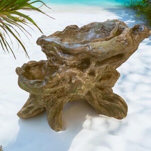 May include: A rustic, brown, wooden bird bath shaped like a tree stump with a large, bowl-shaped top. The bird bath is sitting on a white sandy surface.