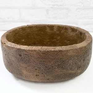 May include: A round, brown, textured ceramic planter with a rough, uneven surface. The planter is empty and ready for planting.