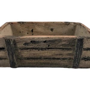 May include: A rectangular, light brown ceramic planter with a rustic wood-grain design. The planter has a slightly raised rim and is perfect for small plants or succulents.