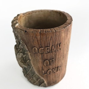 May include: A brown wooden planter with a rope design and the words "Ocean of Love" carved into the side.