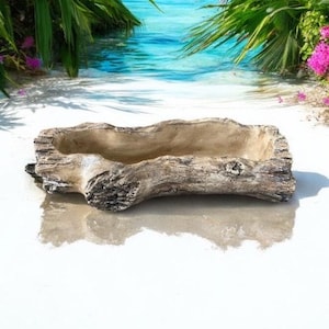 May include: A rustic, light brown, wooden planter with a trough shape. The planter is made to look like a weathered log and is sitting on a white sandy surface.