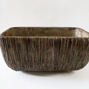 May include: A rectangular concrete planter with a textured, wood-like finish. The planter is brown and has a slightly rounded bottom.