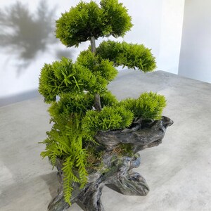 May include: A green artificial bonsai tree in a dark gray wooden planter. The tree has multiple branches and layers of green leaves.