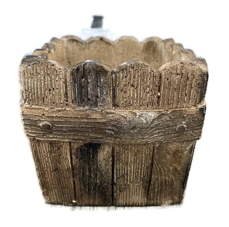 Op de afbeelding: Een vierkante, bruine, houten plantenbak met een decoratief hekwerkontwerp rond de bovenrand.