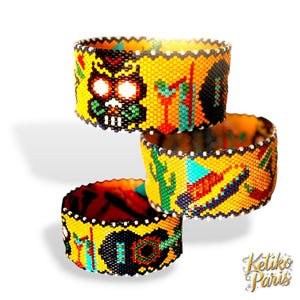 May include: Three beaded bracelets with vibrant yellow, black, red, and turquoise designs. The bracelets feature Day of the Dead skulls, cacti, guitars, and other cultural motifs. The bracelets are stacked on top of each other.