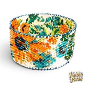 May include: A wide cuff bracelet crafted from tiny glass beads in a floral pattern. The design features vibrant orange, turquoise, and green blossoms against a white background, finished with a dark blue beaded border and the text Ketiko Paris.