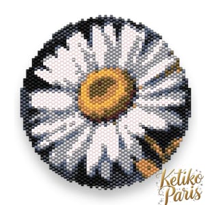 Puede incluir: Un diseño redondo de margarita con cuentas, con pétalos blancos, un centro amarillo y un fondo negro. El diseño es probablemente un broche o parche, que muestra un tema floral. El texto "Ketiko Paris" está en la esquina inferior derecha.