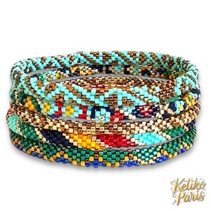 Puede incluir: Una pila de pulseras de cuentas en varios colores, incluyendo turquesa, dorado, rojo y verde. Las pulseras están tejidas con pequeñas cuentas, creando una superficie texturizada. Las pulseras están apiladas una encima de otra.