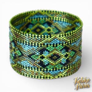Peut inclure: Un bracelet manchette large composé de minuscules perles de verre formant un motif géométrique. Le design présente un motif répétitif dans des tons de vert citron, turquoise, bleu marine foncé et bronze métallique, créant une surface texturée.