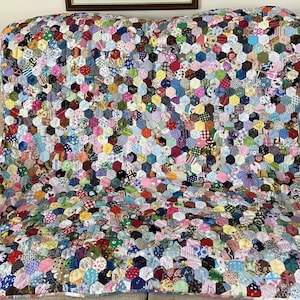 May include: A colourful patchwork quilt made of many different fabric scraps sewn together in a hexagonal pattern. The quilt is made in a variety of colours, including pink, blue, green, yellow, and red.