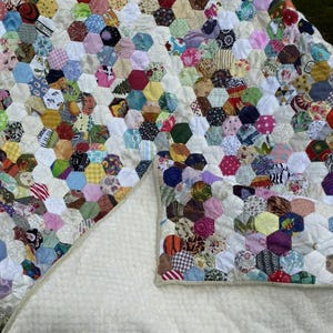 May include: A handmade quilt featuring a patchwork design of colorful hexagonal fabric pieces. The quilt's top is a vibrant mix of patterns and colors, while the underside is a soft, cream-colored material.