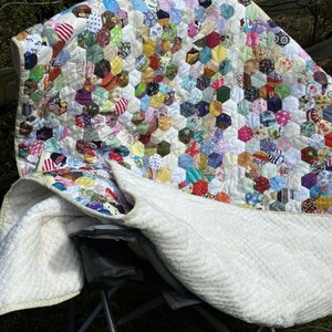 May include: A colorful handmade quilt with a patchwork design of hexagonal fabric pieces. The quilt features a variety of patterns and colors, including red, blue, green, and yellow. The back of the quilt is white.