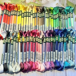 Puede incluir: Una colecci&oacute;n de 60 carretes de hilo de bordar en varios colores, incluyendo rojo, amarillo, verde, azul y morado. Cada carrete tiene una etiqueta blanca con texto negro.