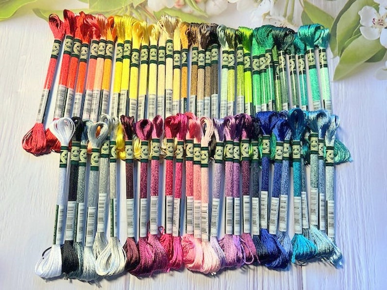 Puede incluir: Una colecci&oacute;n de 60 carretes de hilo de bordar en varios colores, incluyendo rojo, amarillo, verde, azul y morado. Cada carrete tiene una etiqueta blanca con texto negro.