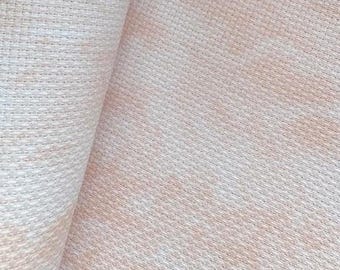 May include: Close-up of a textured fabric with a woven pattern. The fabric has a light beige color with subtle variations in tone, creating a soft, neutral appearance. The weave is visible, adding depth and detail to the material.