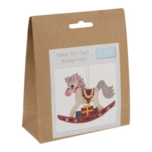 May include: A brown paper package with a white label that says "Make Your Own Rocking Horse" and a small blue label that says "Trimits". The label shows a white rocking horse with pink ears and a silver mane and tail. The horse is holding a stack of wrapped gifts.