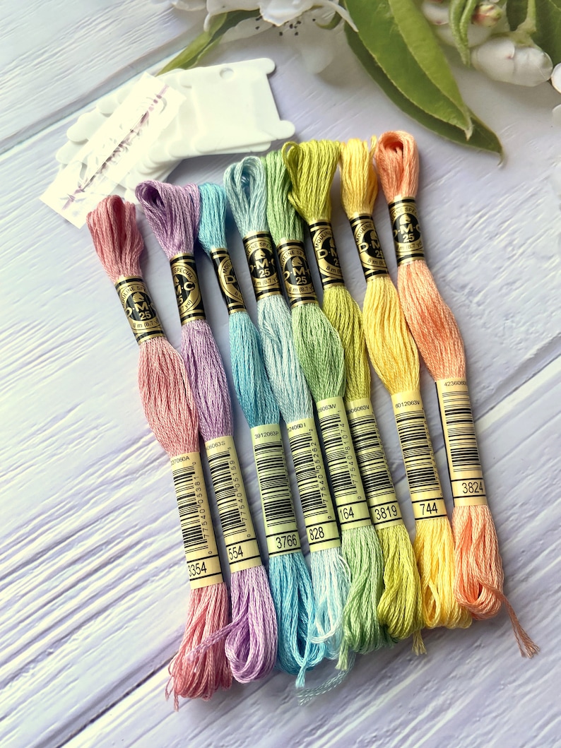 May include: Eight skeins of DMC embroidery floss in pastel colors, including pink, lavender, light blue, green, and yellow. Each skein has a DMC label with a barcode and the DMC number printed on it.
