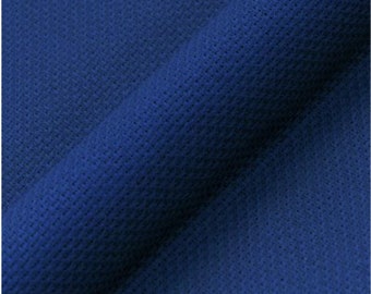 Puede incluir: Una tela de color azul profundo que presenta una superficie texturizada fina, consistente y ligeramente elevada. El material está doblado en diagonal, creando una sombra suave a lo largo del pliegue que resalta el patrón uniforme del tejido.