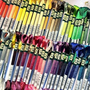 May include: A collection of embroidery floss spools in various colors, including red, orange, yellow, green, blue, purple, and white. The spools are arranged in rows and are labeled with numbers.