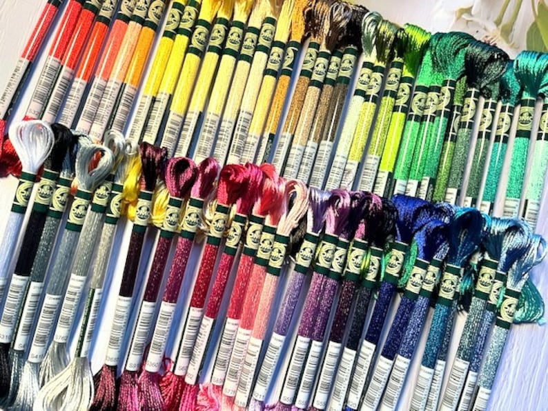 Puede incluir: Una colecci&oacute;n de carretes de hilo de bordar en varios colores, incluyendo rojo, naranja, amarillo, verde, azul, morado y blanco. Los carretes est&aacute;n dispuestos en filas y est&aacute;n etiquetados con n&uacute;meros.