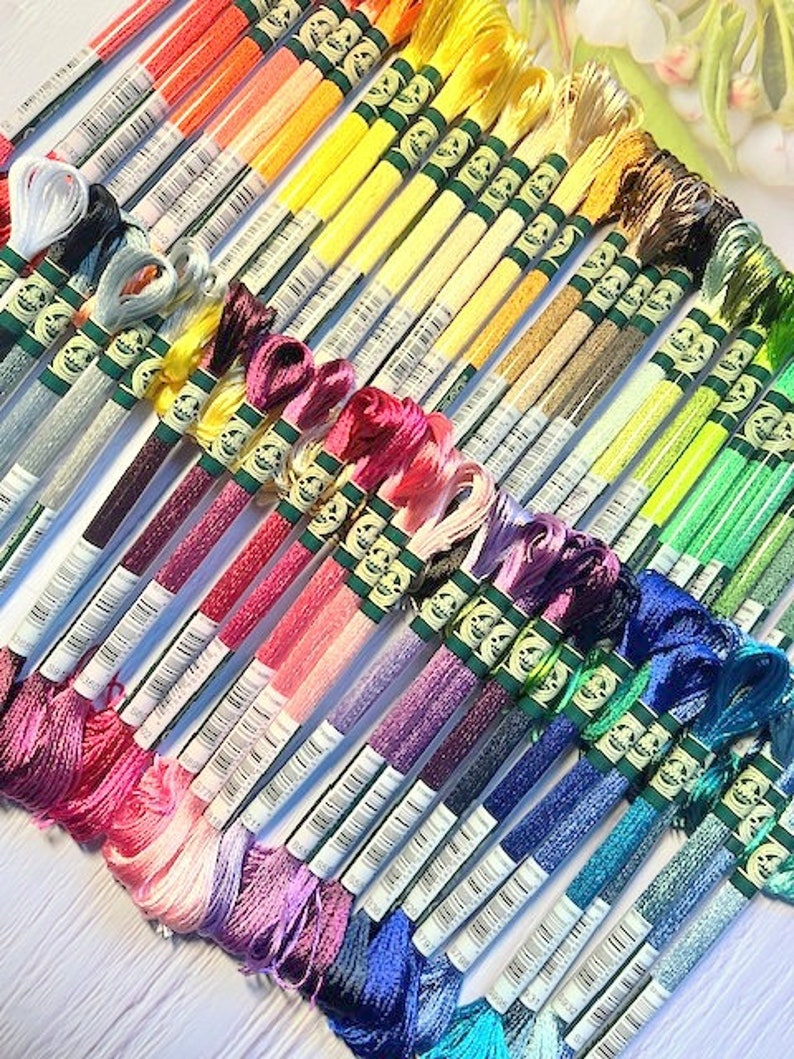 Puede incluir: Una colecci&oacute;n de carretes de hilo de bordar en un arco&iacute;ris de colores, incluyendo blanco, azul claro, rosa, morado, rojo, naranja, amarillo, verde y azul. Los carretes est&aacute;n dispuestos en forma de abanico, con los colores mezcl&aacute;ndose entre s&iacute;.