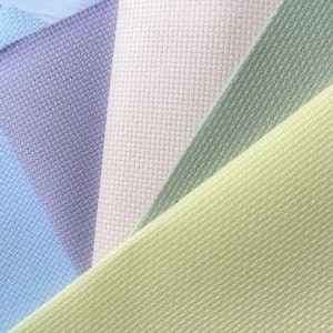 May include: Close-up of a fan of cross-stitch fabric in pastel colors. The fabrics include light blue, lavender, cream, sage green, and pale yellow. The fabric has a textured, woven appearance, ideal for embroidery projects.
