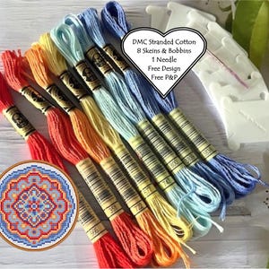 Könnte beinhalten: Ein Set mit acht Knäuelen DMC-Stickstickgarn in einem Regenbogen von Farben, darunter Rot, Orange, Gelb, Hellblau und Dunkelblau. Das Garn ist fächerförmig angeordnet, wobei die Enden der Knäuel sichtbar sind. Das Set enthält außerdem Spulen, eine Nadel und ein kostenloses Design. DMC Stranded Cotton 8 Skeins & Bobbins 1 Needle Free Design Free P&P