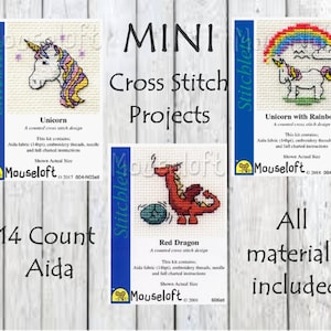 May include: Three mini cross stitch patterns featuring a unicorn, a unicorn with a rainbow, and a red dragon. The patterns are printed on white cards with blue borders and the text "14 Count Aida" and "All materials included".