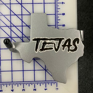 May include: A silver metal Texas-shaped wall hook with a black "TEXAS" sticker. The hook has a small, black metal hook at the top.