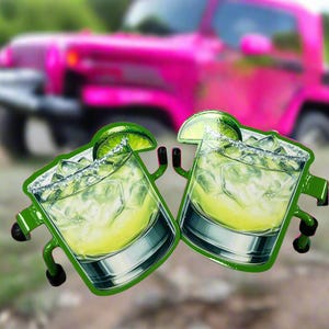 K&ouml;nnte beinhalten: Zwei gestanzte Aufkleber mit Illustrationen von Margaritas in Gl&auml;sern mit Eisw&uuml;rfeln, einem Salzrand und einer Limettenscheibe als Garnitur. Jedes Glas hat kleine gr&uuml;ne Arme und Beine an den Seiten, was ihnen ein charakterartiges Aussehen verleiht.