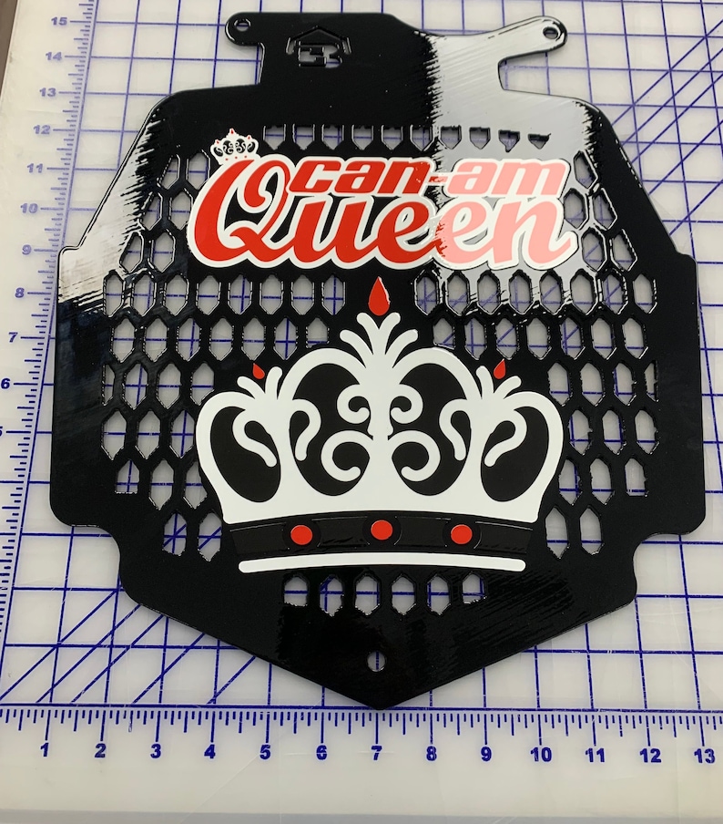 May include: Black metal radiator guard with a white and red crown graphic and the text "Can-Am Queen".