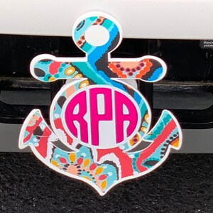 May include: A white anchor-shaped car charm with a pink monogram "RPA" in the centre. The anchor is decorated with a colourful paisley pattern in shades of blue, red, orange, and yellow.