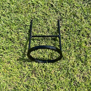 May include: Black metal plant stand with a circular base and two horizontal bars. The stand is on a green grassy surface.