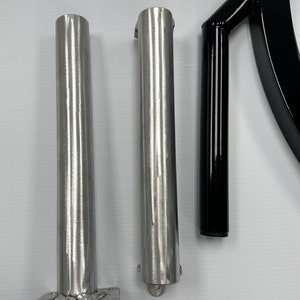 May include: Three metal parts for a piece of exercise equipment. Two silver metal poles with a round base and a black metal pole with a curved handle.