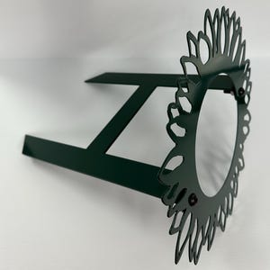 May include: A dark green metal garden stake with a decorative sunflower design. The stake has two legs for stability.