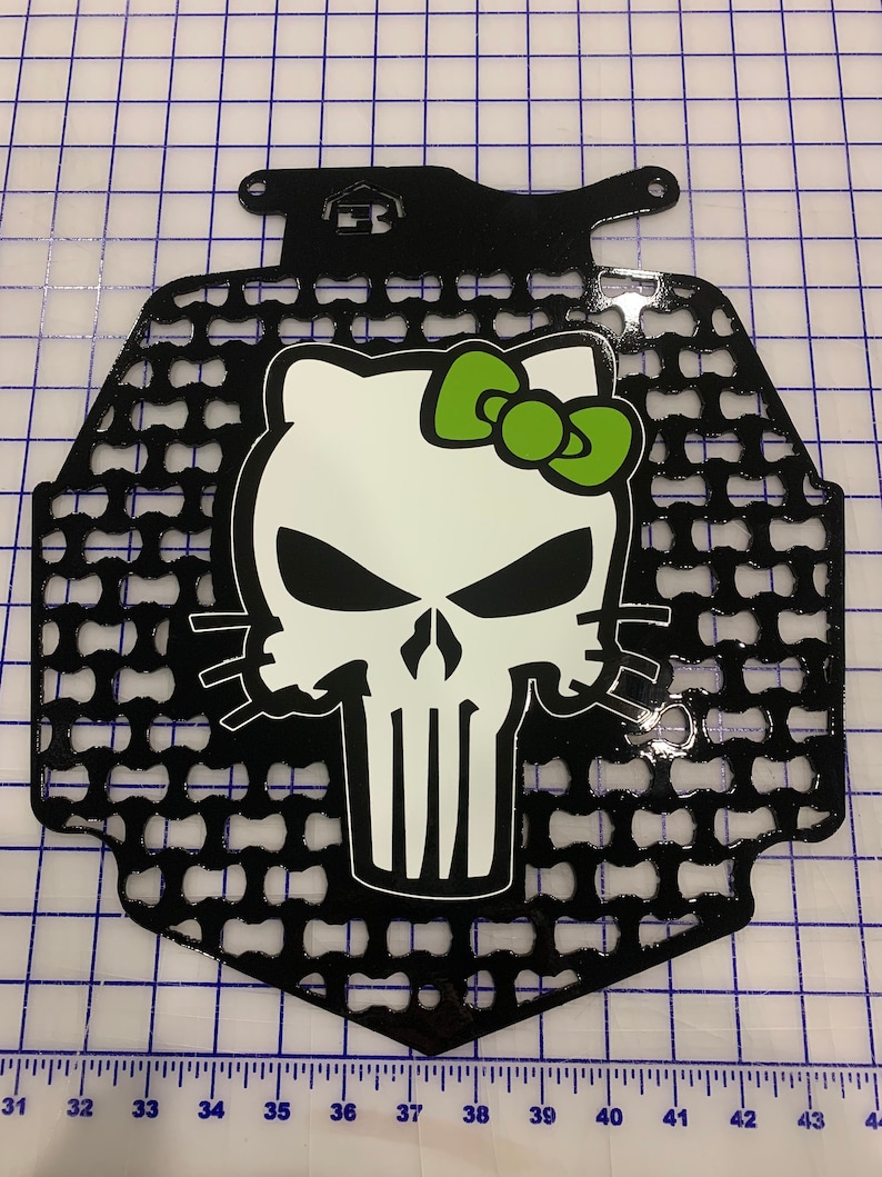 May include: Black metal motorcycle radiator guard with a white and green Hello Kitty skull graphic.