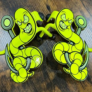 K&ouml;nnte beinhalten: Zwei neon-gelbe Wandhaken aus Metall mit einem Cartoon-Wurm mit w&uuml;tendem Gesichtsausdruck, der sich um einen Angelhaken windet. Jeder Haken hat ein geschwungenes Design mit schwarzen Gummispitzen an den Enden und einer runden Montageplatte.