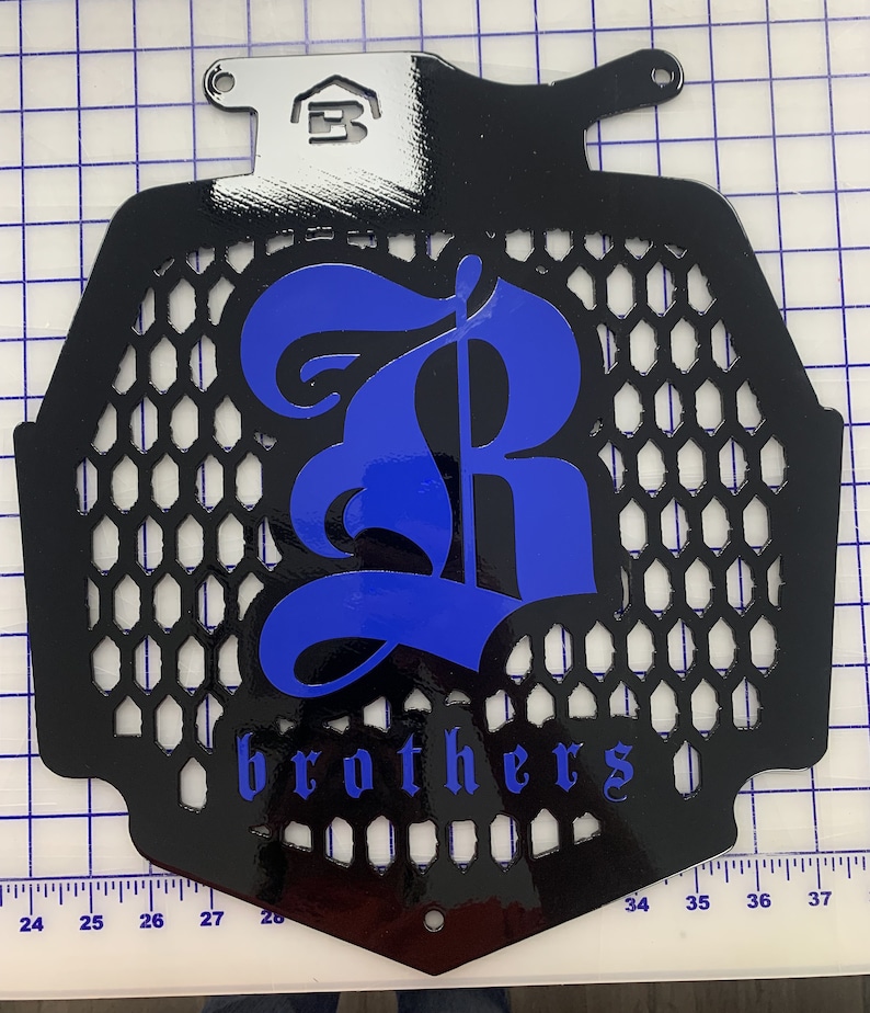K&ouml;nnte beinhalten: Schwarzer K&uuml;hlergrill aus Metall mit einem blauen 'R' und dem Wort 'brothers' in blauen Buchstaben.