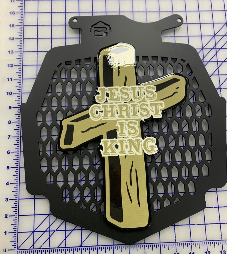 May include: A black metal grille with a gold cross and the words "JESUS CHRIST IS KING" on it.