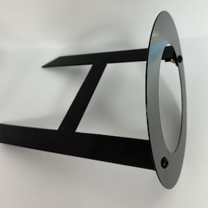 May include: Black metal stand with a round, flat top. The stand has two vertical supports and a horizontal bar connecting them.