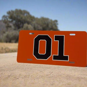 May include: Orange metal license plate with black numbers "01" on a dirt road.
