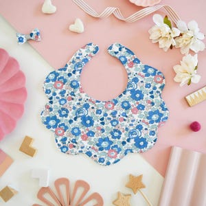 May include: A blue and pink floral print baby bib with a scalloped edge.