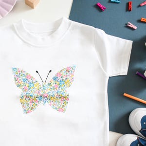 May include: White t-shirt with a floral butterfly design.