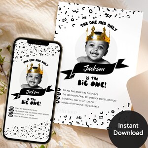 First birthday invitation card and phone screen mockup showing a black-and-white baby photo in a gold crown, with 'The One and Only Jackson is the Big One' text and editable party details, styled with cream fabric, an envelope, and white flowers.