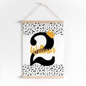 Puede incluir: Un p&oacute;ster imprimible blanco con un n&uacute;mero dos negro y una corona dorada en la parte superior. El n&uacute;mero dos tiene el nombre "William" escrito en &eacute;l. El fondo est&aacute; lleno de formas abstractas en blanco y negro.