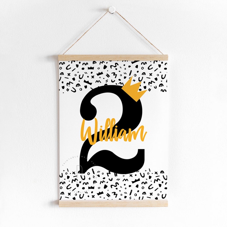 Puede incluir: Un p&oacute;ster imprimible blanco con un n&uacute;mero dos negro y una corona dorada en la parte superior. El n&uacute;mero dos tiene el nombre "William" escrito en &eacute;l. El fondo est&aacute; lleno de formas abstractas en blanco y negro.