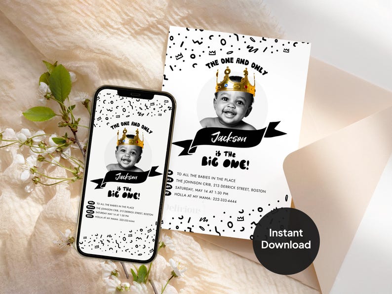 First birthday invitation card and phone screen mockup showing a black-and-white baby photo in a gold crown, with 'The One and Only Jackson is the Big One' text and editable party details, styled with cream fabric, an envelope, and white flowers.