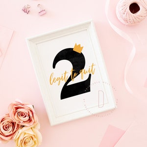 May include: A white framed print with a black number two with a gold crown on top. The text "legit to quit" is written in gold letters.