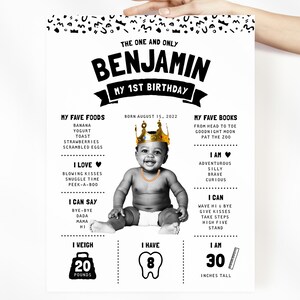 May include: A white birthday milestone poster for Benjamin featuring black text and graphics. It includes a central black and white photo of a baby wearing a gold crown and chain, with sections detailing favorite foods, books, and developmental milestones.